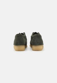 Green suede shoes with a rounded shape, textured finish, and a light brown low heel. Features simple stitching and a minimalist design.