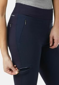 Leggings sportivi navy con un ampio elastico in vita, tessuto testurizzato e due tasche con zip sulle cosce. Le zip sono di tonalità argento.