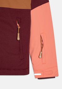 Buntes Jackett in Kastanienbraun und Rosa mit mehreren Paneelen, ausgestattet mit zwei Reißverschlusstaschen mit braunen Zippern, einem Klettverschluss an den Bündchen und einem weißen reflektierenden Detail.