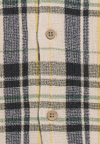 Ruudullinen pellavapaita beige, tummansininen, vihreä ja keltainen. Ominaisuuksiin kuuluu teksturoitu kangas ja puinen nappi napituksessa.