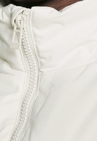 Tejido de chaqueta blanco con una cremallera texturizada que presenta un tirador elevado, mostrando un acabado suave y mate con un sutil detalle en las costuras.