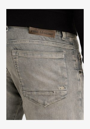 Vista posteriore di jeans denim grigio sbiadito con grande tasca posteriore e etichetta in pelle marrone del marchio PME Legend sulla cintura.