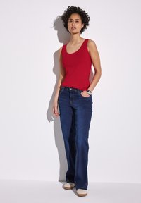 Top rosso abbinato a jeans a zampa d'elefante blu scuro. L'outfit presenta un design semplice, una texture liscia e un aspetto minimalista.