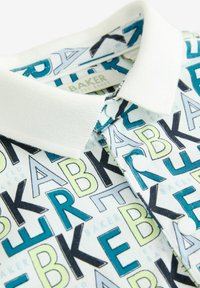Polo tričko s golierom, ktoré má prevažne bielu látku s grafickým vzorom odvážnych písmen v modrej, čiernej a zelenej farbe. Biele gombíky a golier.