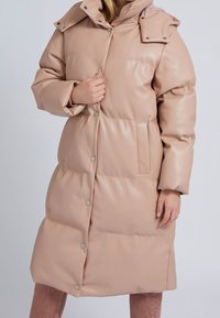 Dunjacka i mjuk rosa med en glänsande yta, stor huva, tryckknappar, sidofickor och knälång design med quiltat mönster.