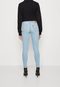 Vaqueros ajustados azul claro con una cintura de altura media, que presentan bolsillos traseros clásicos y una etiqueta de marca de cuero. Combinados con una blusa negra de manga larga.