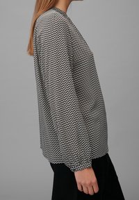 Blus i svart och vitt mönster med långa ärmar, rund halsringning och avslappnad passform. Tyget har en mjuk textur och en subtil glans.