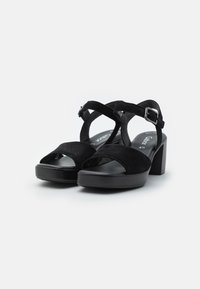 Sandali platform in suede nera con cinturini intrecciati, design aperto all'avampiede e tacco spesso. Presentano una fibbia metallica per la regolazione.