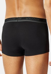 Boxer neri con una morbida cintura elastica che presenta la parola "uncover". Tessuto liscio con una vestibilità aderente e lunghezza fino a metà coscia.