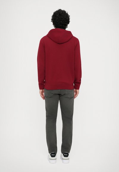 Um moletom bordô com um bolso tipo canguru e um capuz grande, combinado com jeans cinza ajustados e ténis brancos com um logótipo preto.