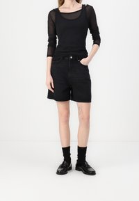 Černý dlouhý rukáv z síťoviny navrstvený na černém tílku, spárovaný s černými džínovými šortkami do délky kolen. Nosené s černými ponožkami a botami.