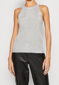 Srebrny halter top z żebrowanym wzorem i dopasowanym krojem. Tkanina ma metaliczny połysk, w zestawieniu z czarnymi skórzanymi spodniami. Prosty i elegancki wygląd.