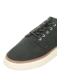 Black canvas shoe with a rounded toe, white sole, and brown accents along the edge. Features eyelets and symmetrical lacing.