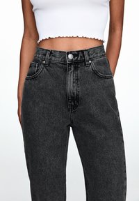 Czarne dżinsy z wysokim stanem i prostą nogawką, wyposażone w przednie kieszenie, zapięcie na guziki oraz subtelne przetarcia w strukturze tkaniny.