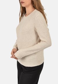 Maglione beige con scollatura tonda, tessuto testurizzato e piccole paillettes sparse. Maniche aderenti e orlo a costine.