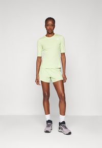 Lys grønne trenings topp med korte ermer, kombinert med matchende shorts. Brukes med grå og svarte tursko og hvite sokker. Enkelt design.