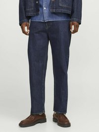 Pantaloni din denim albastru închis cu croială dreaptă, având cusături contrastante, buzunare laterale și tiv uzat. Asortați cu pantofi din piele maro.