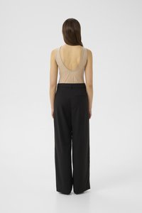 Body beige senza schienale con texture in rete abbinato a pantaloni neri a vita alta e gamba larga, con una sola tasca sul retro.