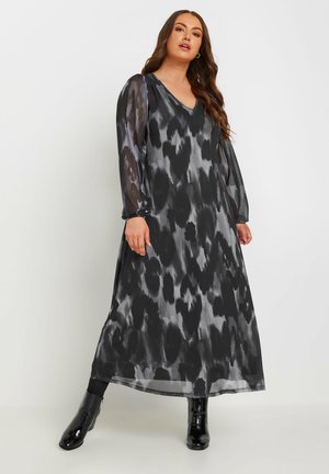 Transparante zwarte en grijze maxi-jurk met een V-hals, lange mouwen en abstract patroon; gestyled met glanzende zwarte kniehoge laarzen.