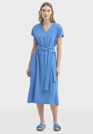 Robe bleue mi-longue jusqu'aux genoux, avec un col en V, des manches courtes, un tissu texturé et une ceinture assortie à la taille ; portée avec des sandales bleues.