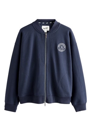 Jachetă bleumarin cu fermoar, guler, manșete și tiv cu striații și logo circular alb „SELF STUDIOS EST. 2023” pe pieptul stâng.