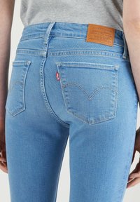 Světlé modré džíny z denimu s mírným vzestupem v pase, designem pěti kapes a charakteristickým křivkovým šitím na zadních kapsách. Kožená nášivka na pase.