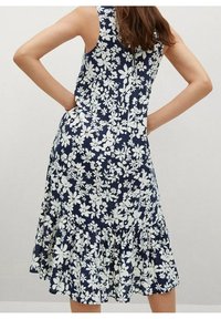 Robe florale marine avec des motifs de fleurs blanches, design sans manches, ourlet à volants et fermeture éclair au dos. Tissu doux et léger.