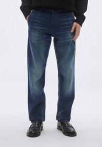 Tumesinised teksad kerge pleekimisega. Sirge lõige, küljetaskud ja vööaasad. Kombineeritud mustade loafers-kingadega.