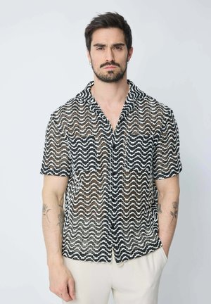 Chemise à manches courtes en tissu tissé avec un motif zigzag noir et blanc. Elle comprend un col et une fermeture avant à boutons.