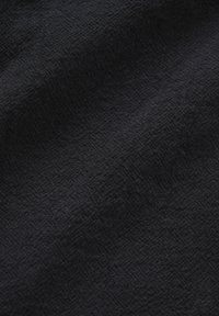 Zwarte stof met een subtiel geweven visgraatpatroon en lichte plooien die zachte schaduwen en textuur creëren.