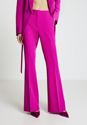 Pantaloni sartoriali fucsia con design a gamba larga, texture liscia, tasche frontali e chiusura con un solo bottone, abbinati a décolleté appuntite dello stesso colore.