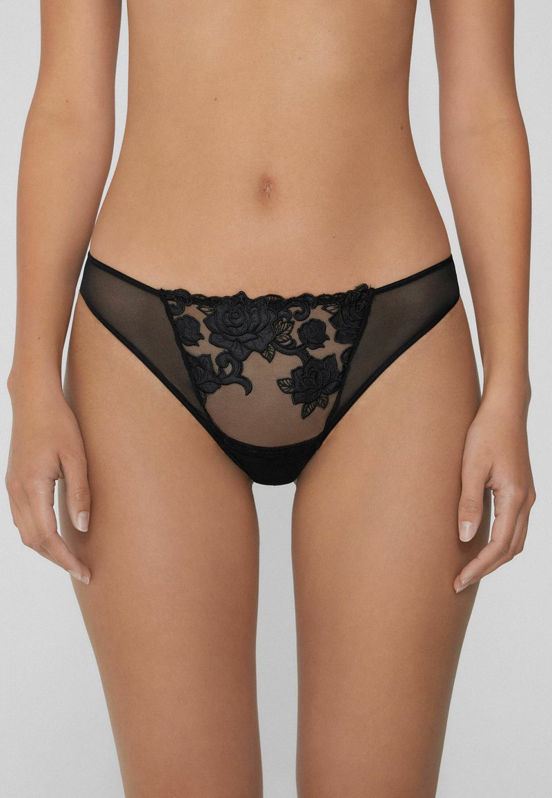 Schwarzer Netz-Tanga mit floralen Spitzen-Details an der Vorderseite, weichem Bund und minimaler Rückendeckung. Strukturierter floraler Print.