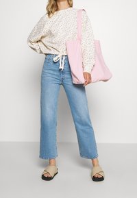 Světle růžová plátěná taška, svetr s květinovým vzorem, široké modré džíny, béžové sandály na klínku s křížovým páskem.