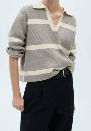 Persona vistiendo un suéter de punto a rayas beige y crema con un escote en V profundo y pantalones negros de talle alto con un cinturón negro.