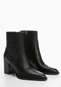 Par de botas de cuero negro hasta el tobillo con puntas afiladas, tacones de bloque y Cremalleras laterales, exhibidas sobre un fondo blanco.