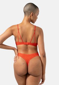Ensemble de lingerie en dentelle rouge comprenant un bralette avec de fines bretelles et une fermeture à crochets, associé à un string assorti rehaussé de dentelle.