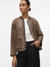 Woman wearing leopard print jacket over white top, with black pants, styled hair, and large silver hoop earrings.
