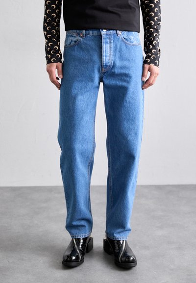 Jeans in denim blu con una vestibilità rilassata, caratterizzati da un classico design a cinque tasche, leggere scuciture e dettagli cuciti. Abbinati a scarpe nere.