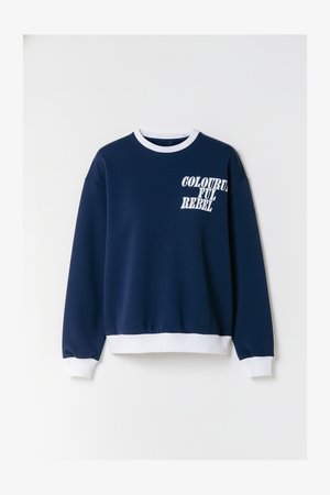 Tumši zils džemperis ar baltu ribveida apkakli un aprocēm. Kreisajā krūšu pusē ar baltu tekstu "COLORFUL REBEL". Mīksts auduma tekstūra.