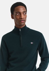 Dunkelblauer Zip-Kragen-Pullover aus weichem Strickmaterial mit einem kleinen Logo auf der Brust und einem gerippten Kragen.