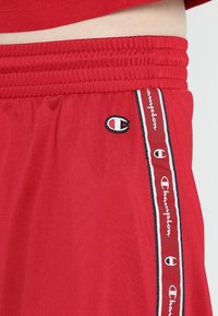 Czerwone sportowe szorty z elastycznym pasem, bocznymi pasami z białymi i czarnymi akcentami oraz małym haftowanym logo.