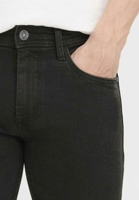 Jeans din denim negru cu un design slim fit. Prezintă buzunare frontale, închidere cu nasture și detalii de cusătură pe talie și pe cusături.