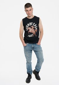 Black sleeveless T-shirt featuring a graphic print of a horse and rider, paired with light blue jeans and black leather boots.