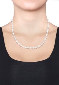 Collier en perles blanches composé de perles rondes de taille uniforme, enfilées en un seul brin, porté sur un haut noir.