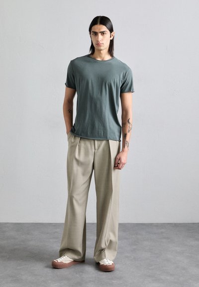 Light green short-sleeve t-shirt, relaxed fit, paired with beige pleated trousers. Brown and white sneakers complete the outfit.