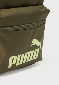 Ελαιώδης πράσινο σακίδιο με υφή, με εμφανές λευκό λογότυπο Puma και φερμουάρ σε θήκη.