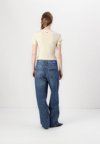 Ανοιχτό μπεζ εφαρμοστό μπλουζάκι με κοντά μανίκια σε συνδυασμό με φαρδιά, μεσαίου μπλε τζιν παντελόνια που διαθέτουν μπλε ετικέτα με λογότυπο στη πίσω μέση.