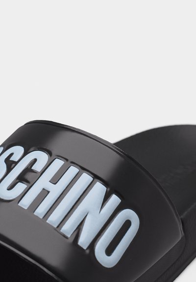 Μαύρο σανδάλι με φαρδιά λουρί που διαθέτει ανάγλυφα μπλε και λευκά γράμματα "MOSCHINO" στην επιφάνεια.