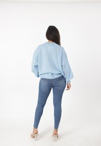 Suéter de punto extragrande en azul claro con cuello redondo, combinado con jeans ajustados azul y sandalias de tacón bloque transparente. Fondo neutro.