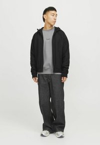 Schwarze Zip-Hoodie über einem grauen Sweatshirt, kombiniert mit lockeren, dunklen Jeans. Die Schuhe haben graue und silberne Akzente. Einfaches, lässiges Design.